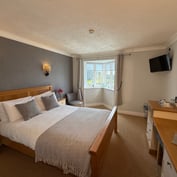 Wider view of the river-view room — feature wall, oak bed and bay window onto Strand Quay