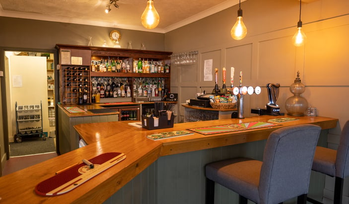 The licensed bar at The River Haven Hotel — Edison-bulb pendants over a wooden bar with stools