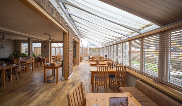 The conservatory breakfast restaurant — wooden tables, slatted blinds and a vaulted glass roof