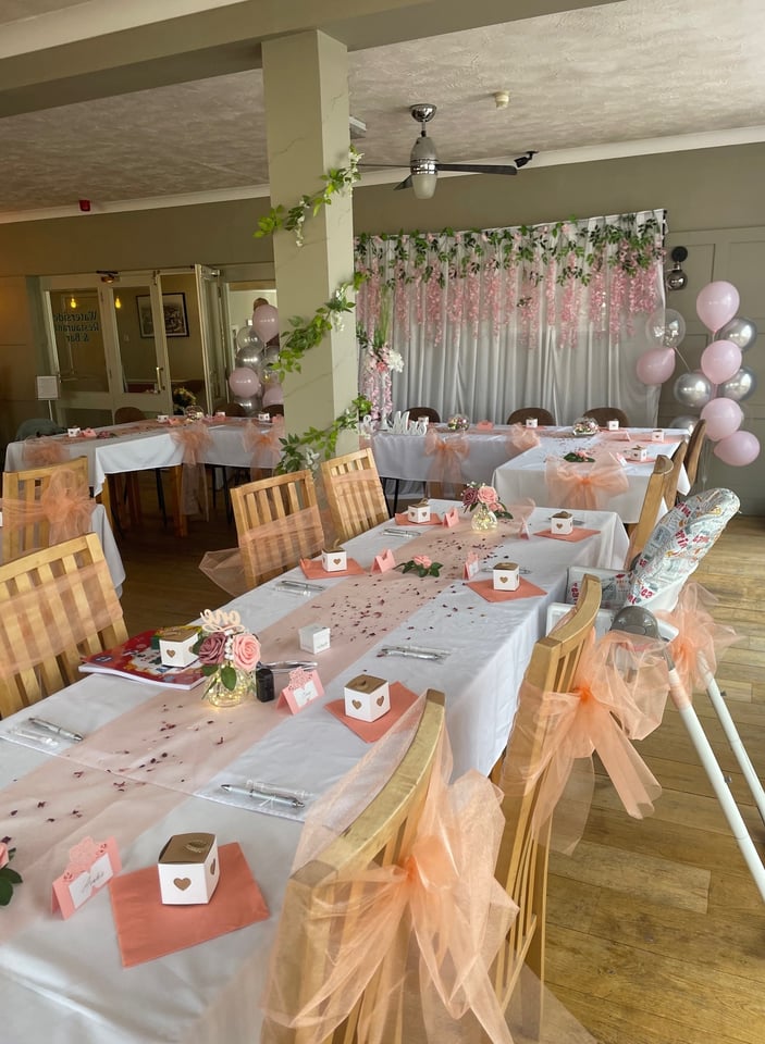 The function room set up for a celebration with peach tulle, balloons and a long banquet table