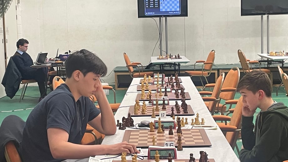 Two young players at adjacent boards in the main playing hall at Horntye Park, with rows of chess sets and live-board screens behind them