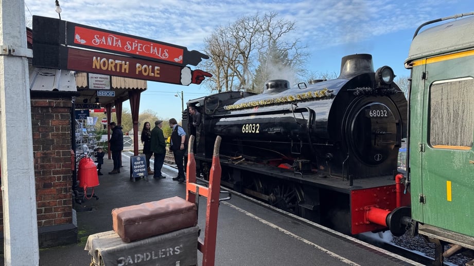 Steam locomotive 68032, trimmed with a gold garland, waits at the Tenterden Town platform beneath a red Santa Specials sign pointing to the North Pole
