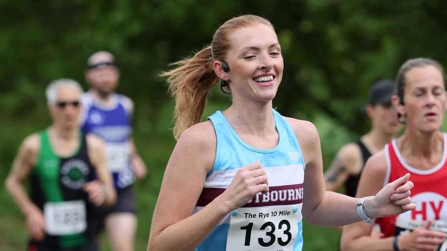 A smiling runner in a race vest and number leads a group of club runners along a tree-lined country lane