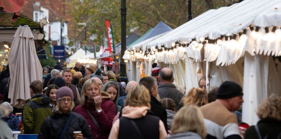 Crowds of shoppers in winter coats walk between a long row of white market marquees hung with festoon lights on Tenterden High Street